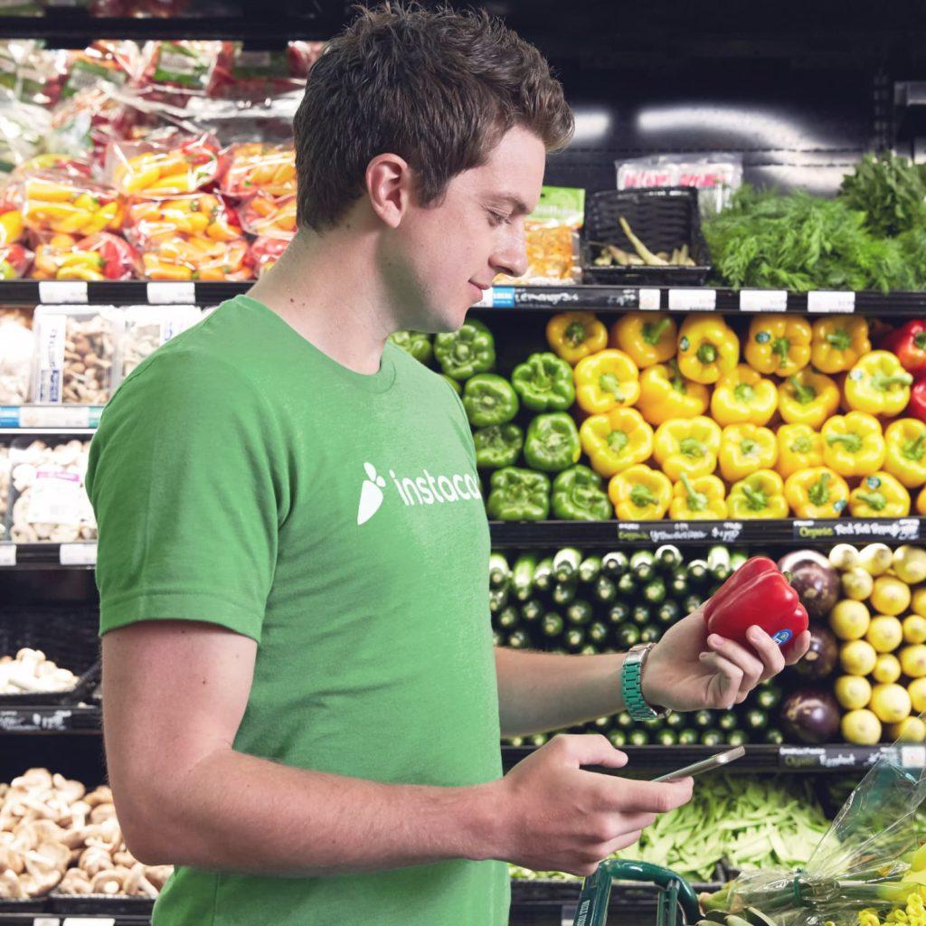 An Instacart shopper holding a pepper in front of the produce aisle.