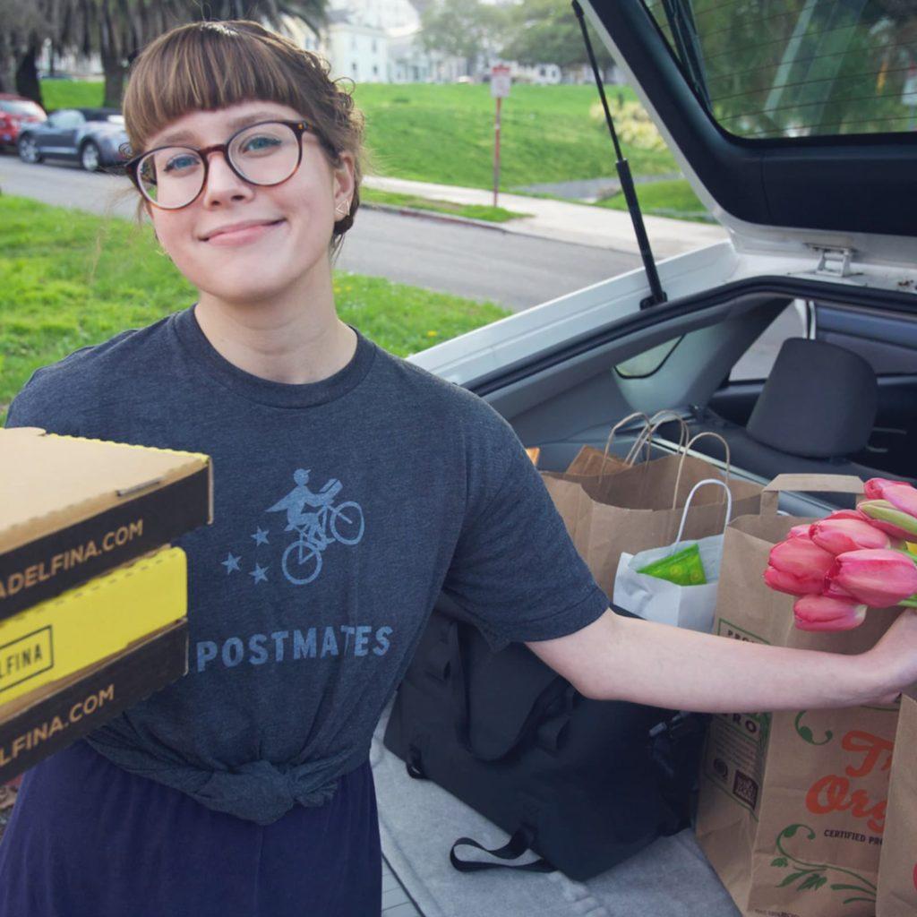A Postmates driver in front of a full truck, holding several pizza boxes.